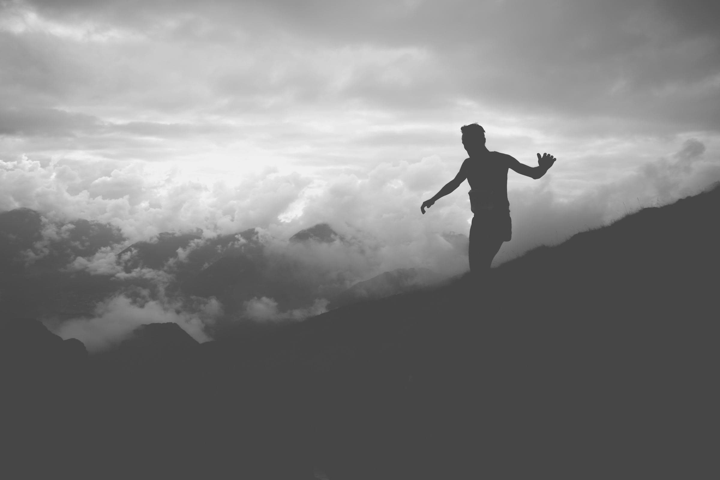 Silueta de un corredor en una ladera de montaña sobre un mar de nubes, en blanco y negro.