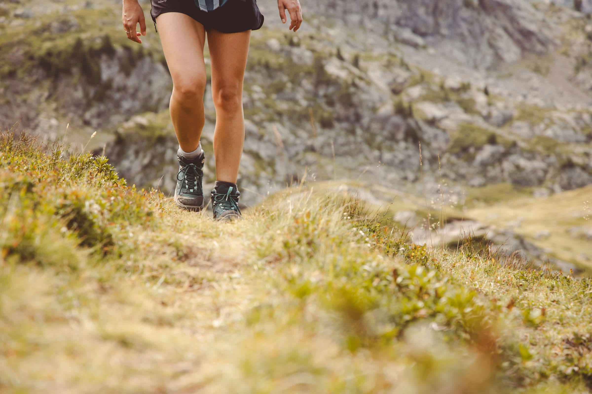 Piernas de una deportista avanzando por un sendero de hierba en la montaña.